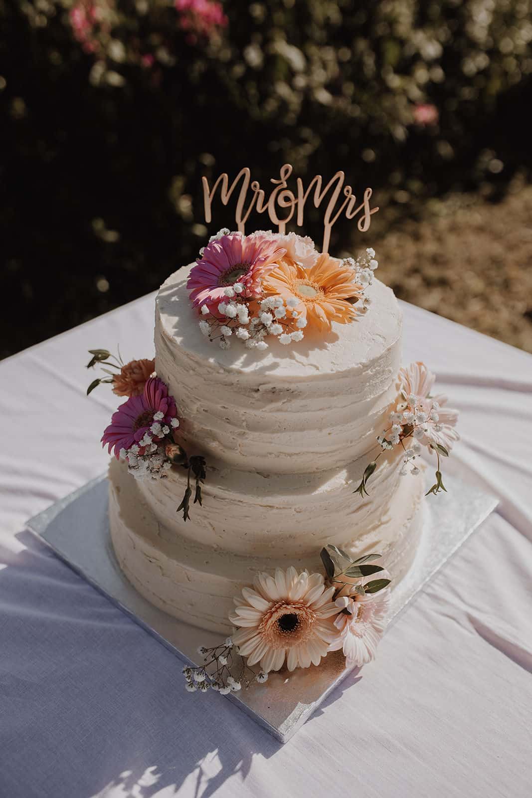 Bryllupskake i tre etasjer med blomster og Mr & Mrs-pynt